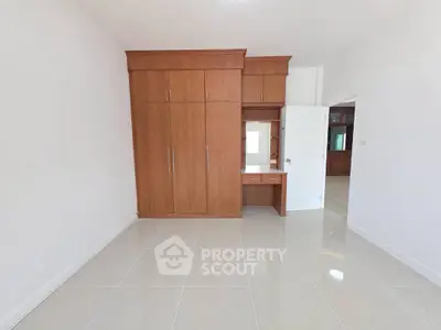 Spacious bedroom with built-in wooden wardrobe and glossy tiled floor, perfect for modern living.