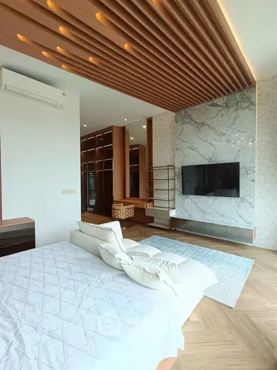 Luxurious modern bedroom with elegant wood paneling and marble accent wall, featuring a large TV and stylish decor.