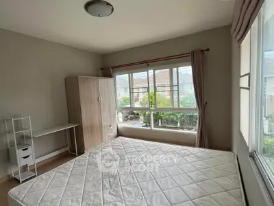 Spacious bedroom with large window and garden view, featuring a wardrobe and desk.