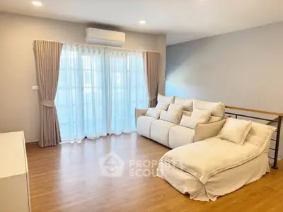 Spacious living room with cozy white sofa and large windows with curtains, featuring elegant wooden flooring.