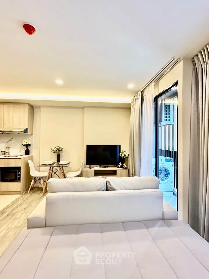 Modern living room with open kitchen and balcony, featuring stylish decor and natural light.
