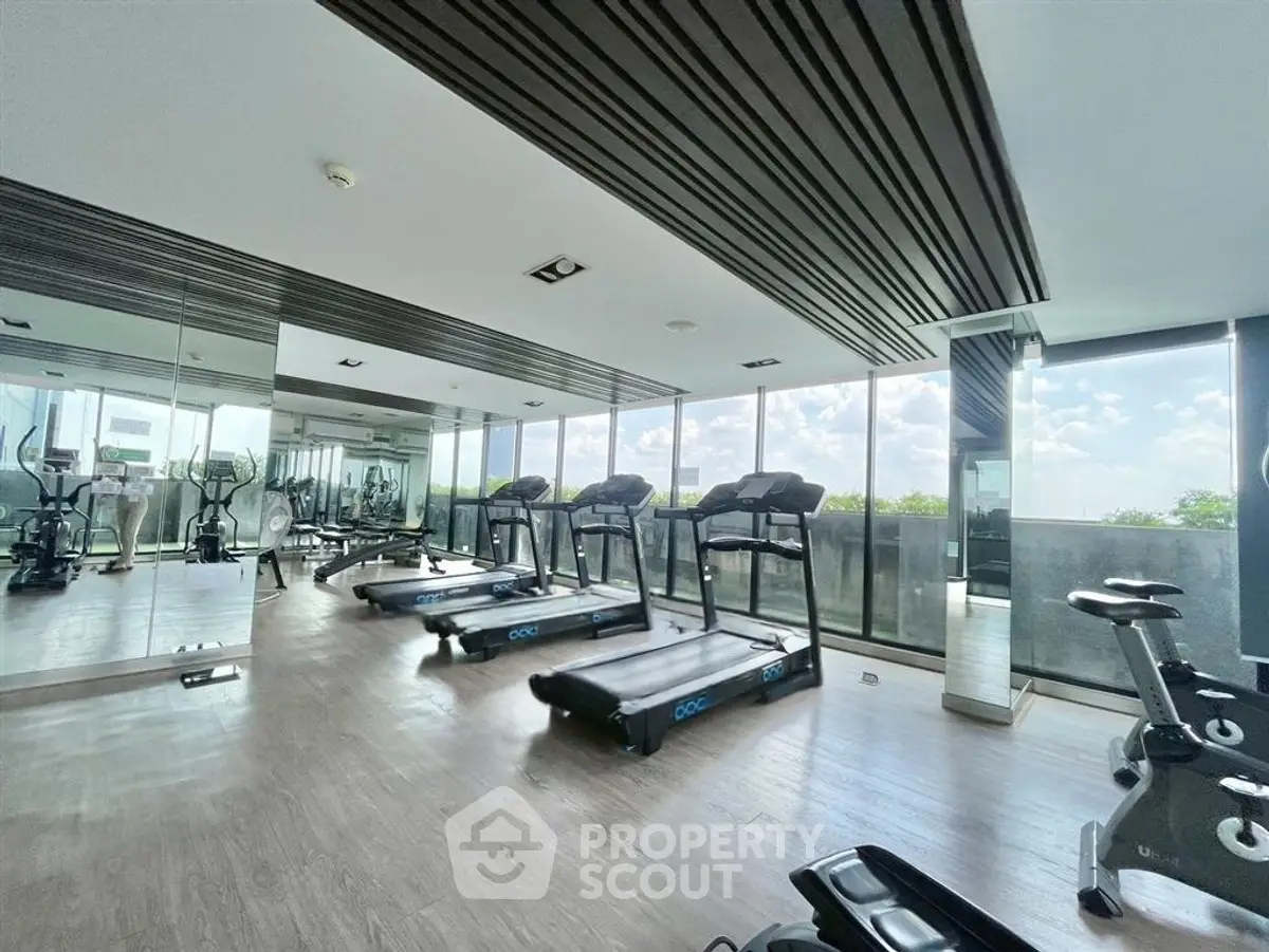 Spacious modern gym with large windows and state-of-the-art equipment in a luxury building.