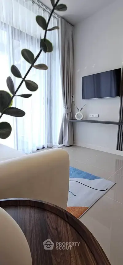 Modern living room with sleek decor, large window, and wall-mounted TV, offering a bright and inviting atmosphere.