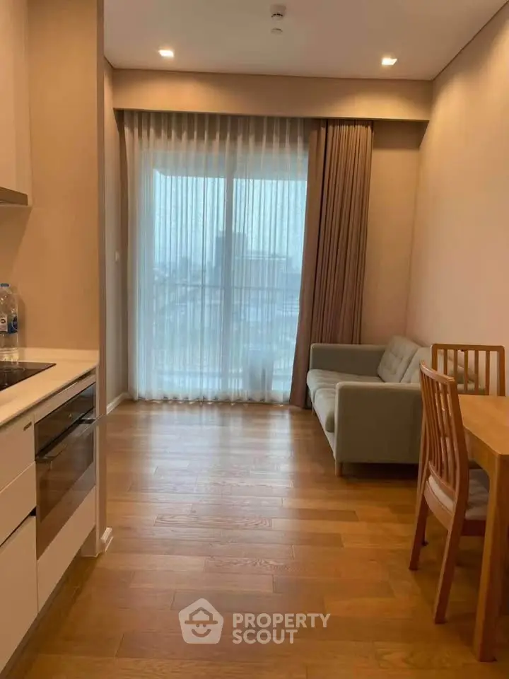 Modern apartment interior with cozy living area and kitchen, featuring wooden flooring and large window.