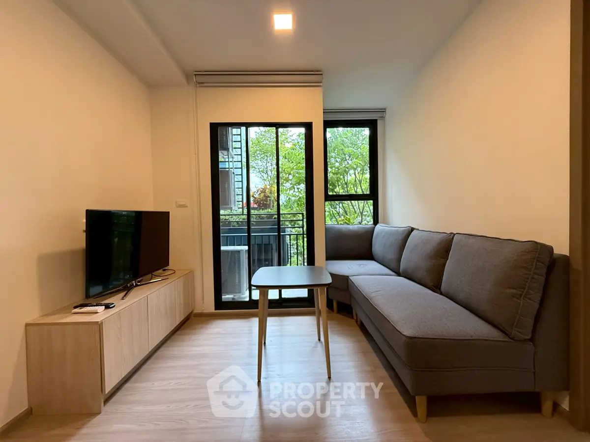 Modern living room with cozy sofa and TV, featuring a view of lush greenery through large windows.