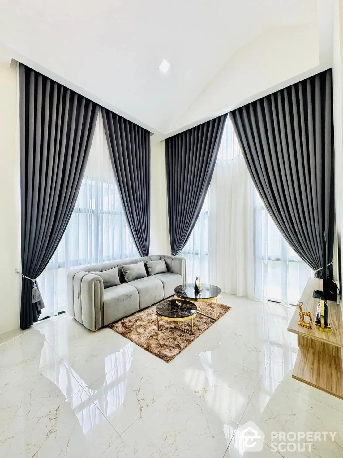 Luxurious living room with high ceilings, elegant marble flooring, and dramatic floor-to-ceiling curtains, showcasing a modern aesthetic with a plush sofa and chic coffee table.