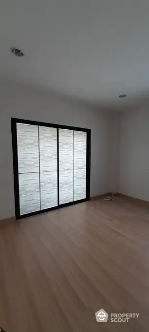 Spacious and modern living room with large frosted glass windows offering privacy and ample natural light, featuring sleek wooden flooring and a neutral color palette for a serene ambiance.