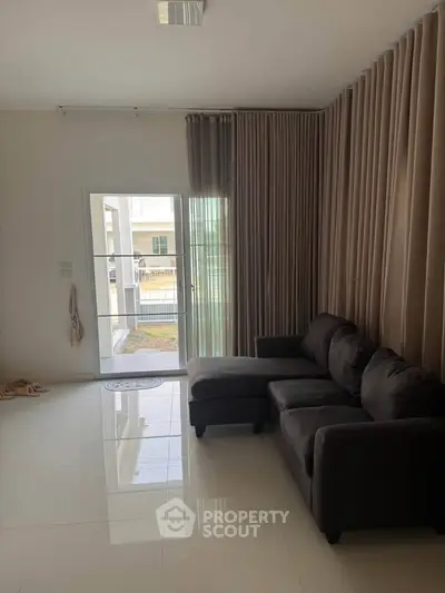 Spacious living room with modern sofa and large window leading to outdoor area.