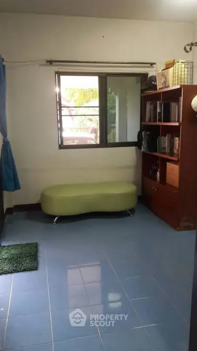 Cozy room with blue tiled floor, green sofa, and wooden bookshelf by the window.