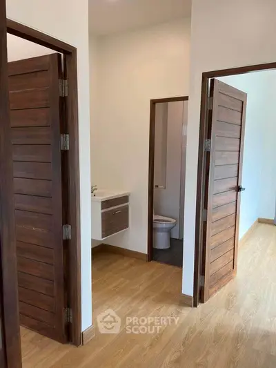 Spacious and modern home interior featuring elegant wooden doors leading to a bright bathroom and a cozy room with warm-toned flooring.