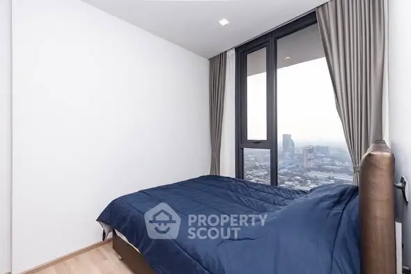 Modern bedroom with large window offering stunning city view, featuring elegant curtains and cozy bedding.
