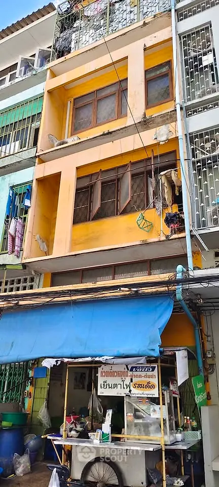 Vibrant yellow multi-story building with street food stall in urban setting.