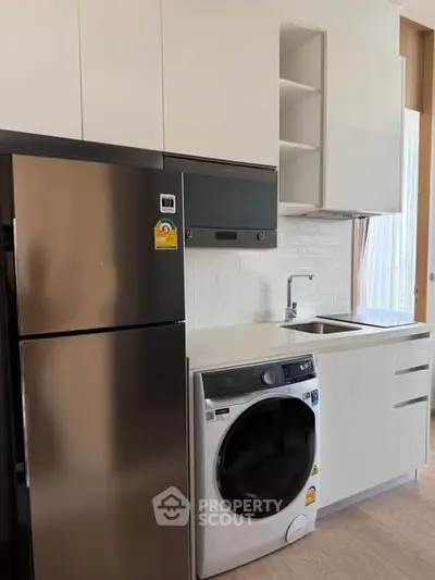 Modern kitchen with sleek appliances including fridge and washing machine, stylish cabinetry, and natural light.