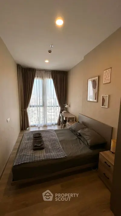 Cozy bedroom with modern decor and large window offering natural light and city view.