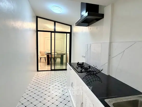 Sleek modern kitchen with black countertop and glass partition, leading to a bright dining area.