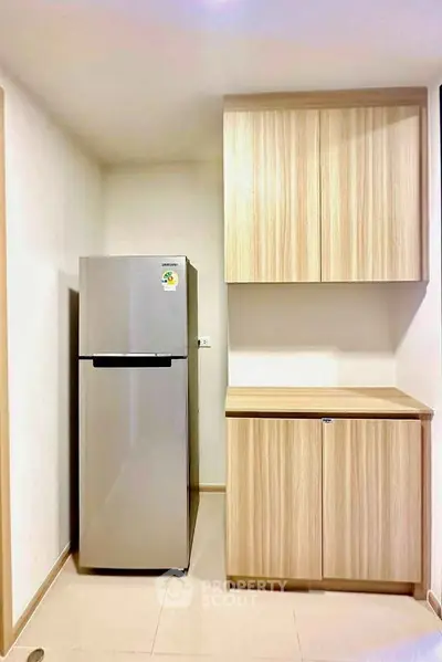 Modern kitchen with sleek fridge and wooden cabinets in a compact layout.