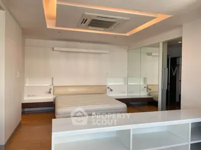 Spacious modern bedroom with built-in lighting and mirrored wall, perfect for luxury living.