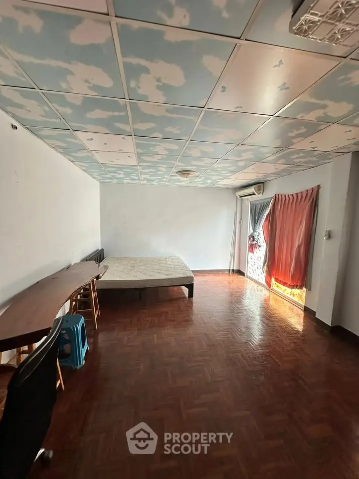 Spacious bedroom with unique cloud ceiling and parquet flooring, featuring a large window for natural light.