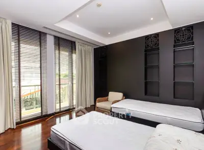 Spacious bedroom with large windows and elegant dark accent wall, featuring two beds and a cozy chair.