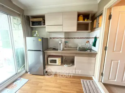 Modern compact kitchen with wooden cabinets, microwave, and fridge in cozy apartment.
