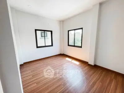 Spacious empty room with wooden flooring and large windows for natural light.