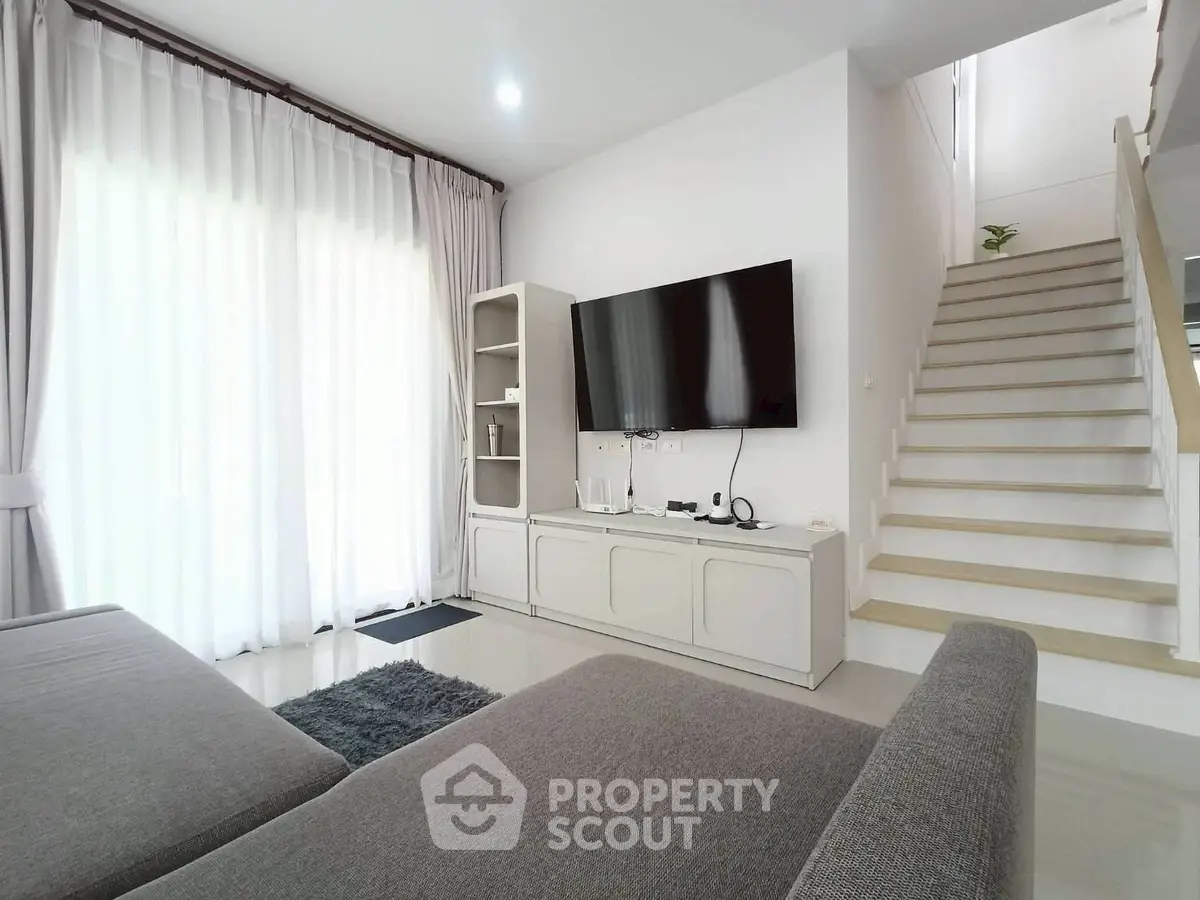 Modern living room with sleek design, large TV, and elegant staircase, perfect for contemporary living.