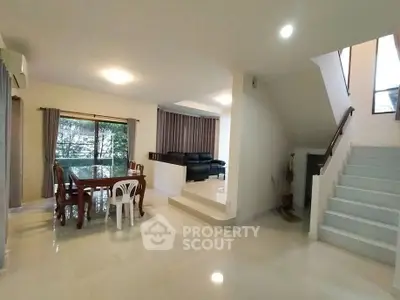 Spacious open-plan living and dining area with modern staircase and large windows.