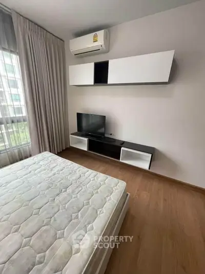Modern bedroom with sleek furniture and natural light, featuring a wall-mounted TV and air conditioning.