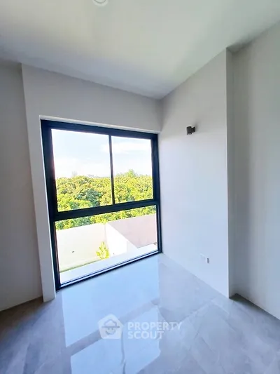 Bright room with large window offering lush green view, perfect for a serene living space.