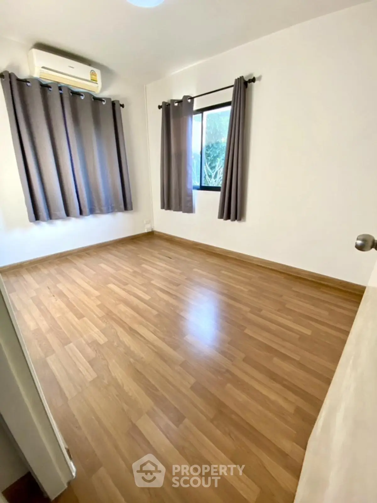Spacious empty bedroom with wooden flooring and large windows for natural light.