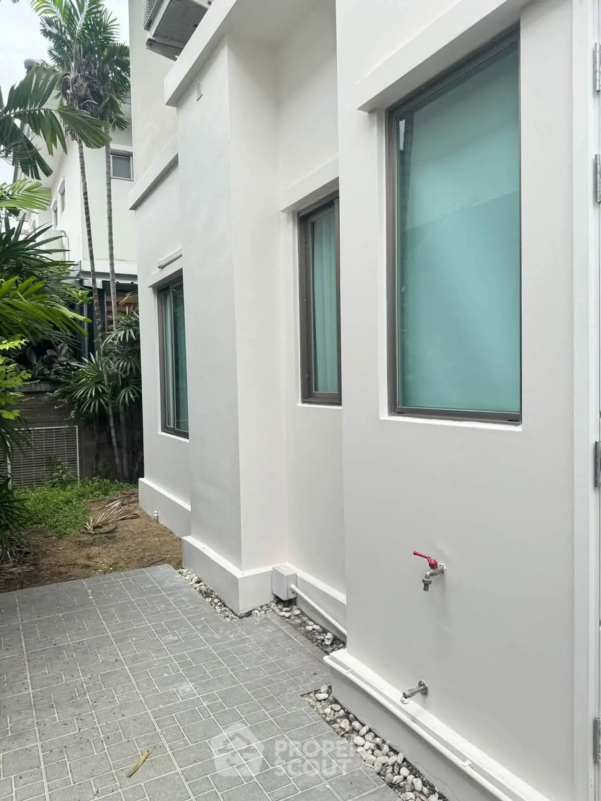 Modern white exterior of a residential building with lush greenery and paved walkway.