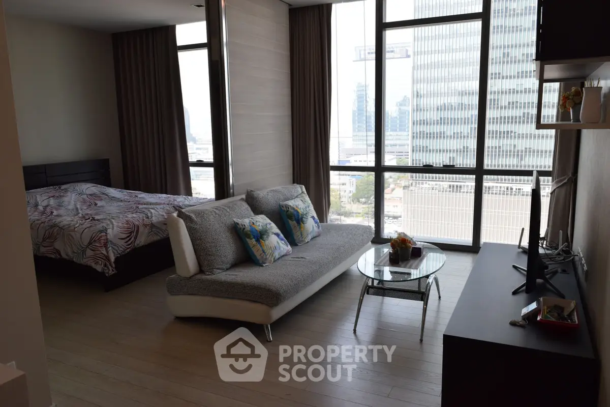 Modern studio apartment with floor-to-ceiling windows and stylish decor in urban setting.