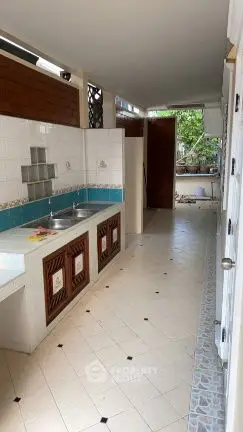 Spacious kitchen with open layout and dual sinks, featuring tiled flooring and wooden cabinets.