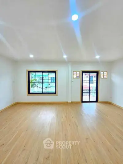 Spacious empty room with wooden flooring and large windows for natural light.