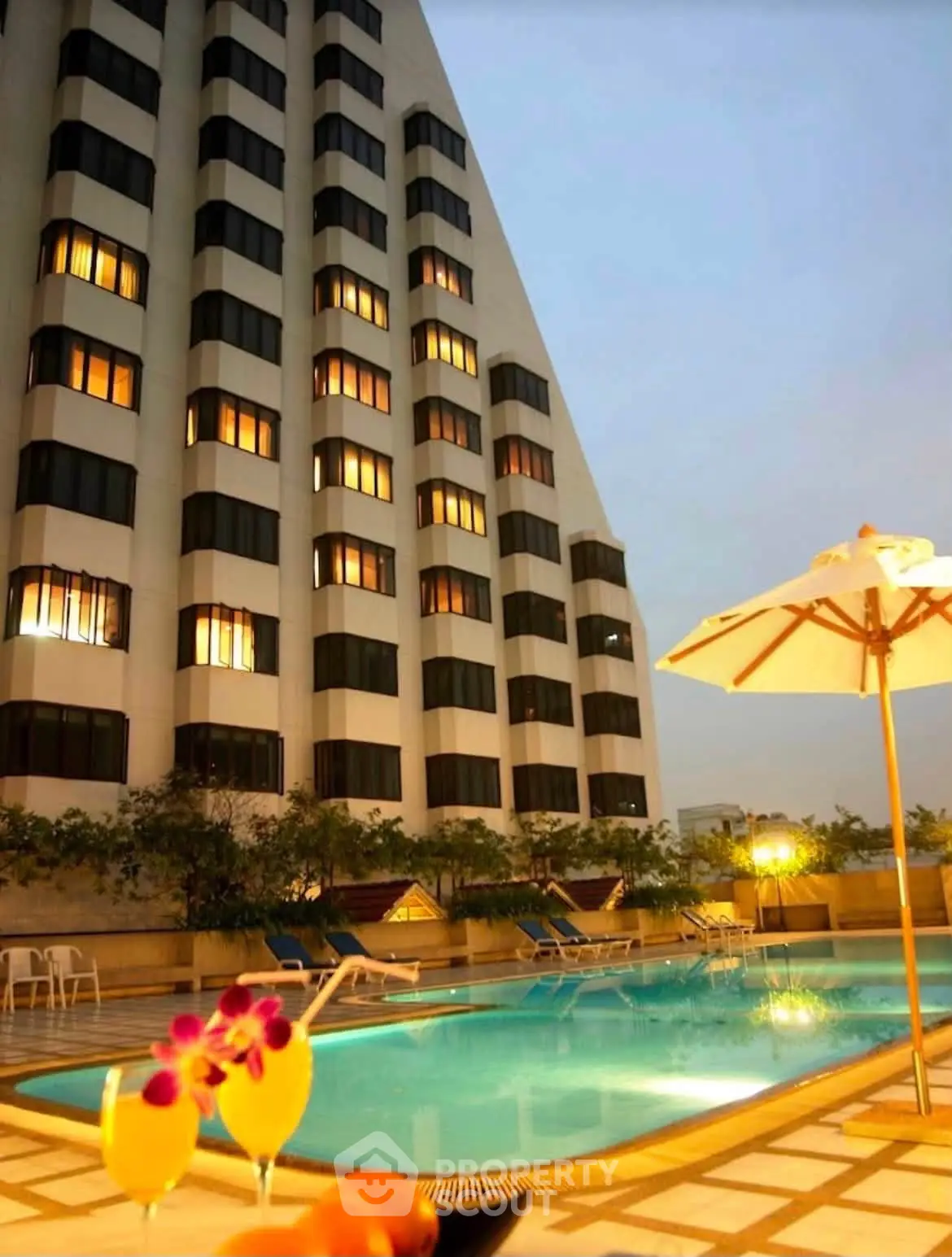 Luxurious high-rise building with illuminated windows and inviting poolside ambiance at dusk.