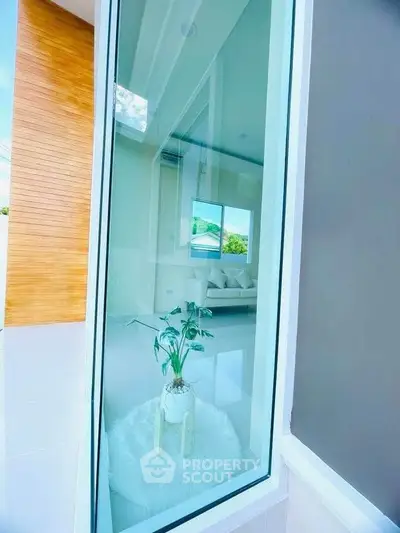 Modern interior view through large window showcasing stylish living room with elegant decor and natural light.