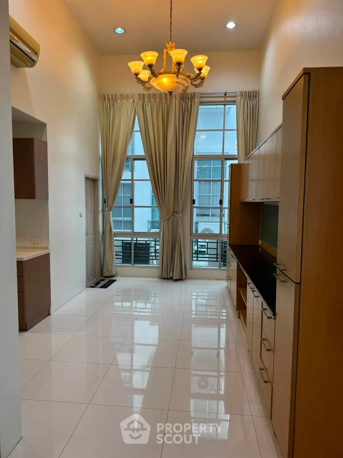Spacious high-ceiling living room with elegant chandelier and large windows.