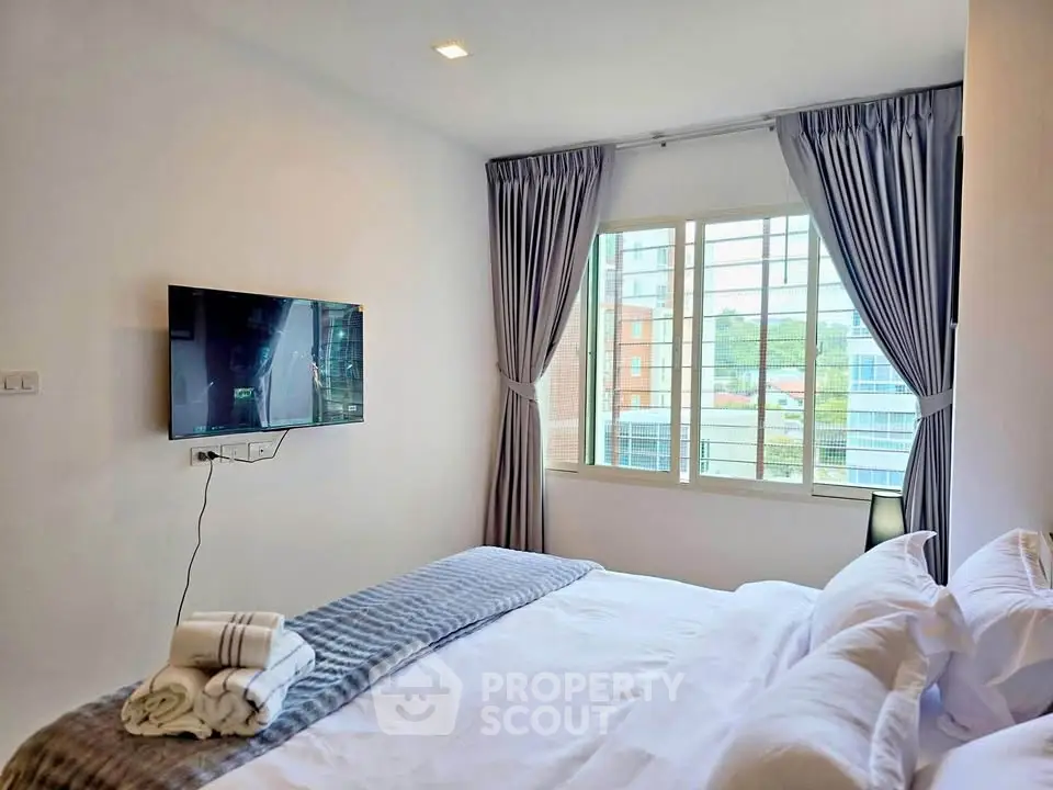 Cozy bedroom with modern decor, featuring a wall-mounted TV and large window with city view.