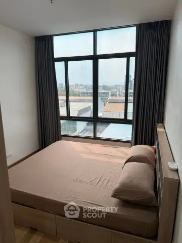 Cozy bedroom with large window offering city views, featuring a comfortable bed and modern decor.