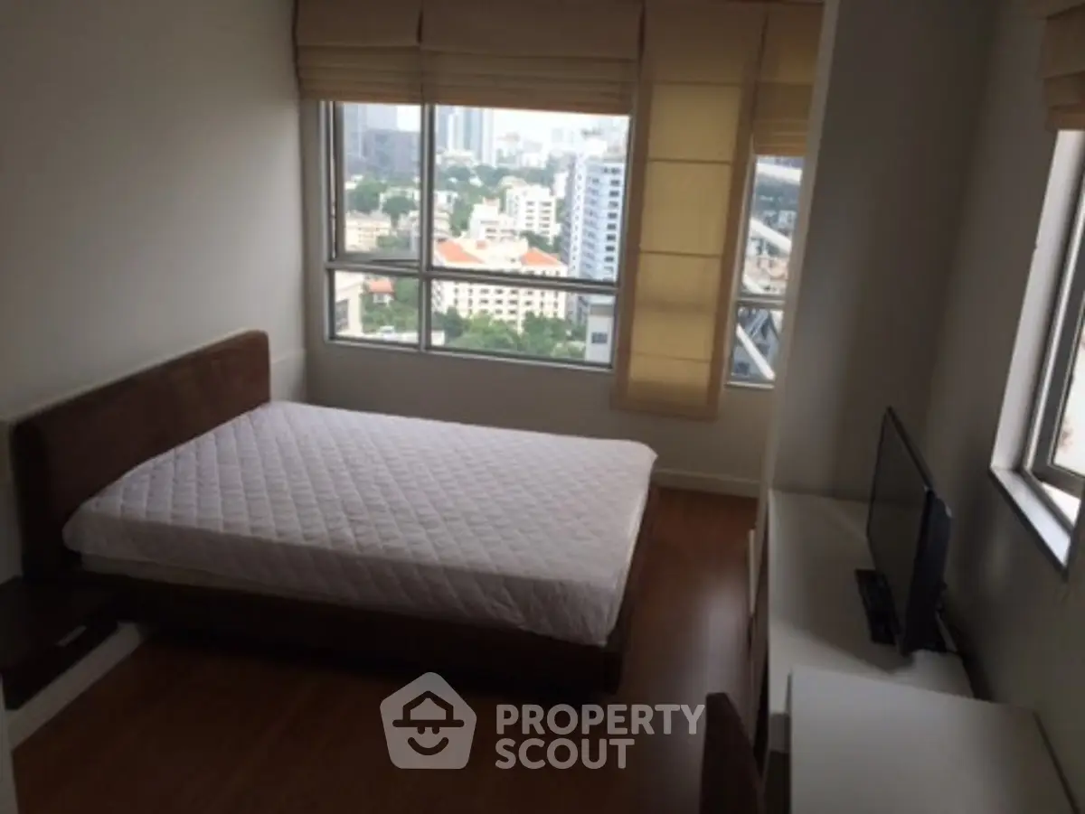 Cozy bedroom with city view, featuring a comfortable bed and large windows for natural light.