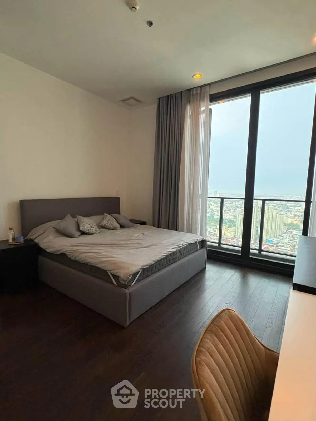 Spacious bedroom with large window offering stunning city views in modern apartment.