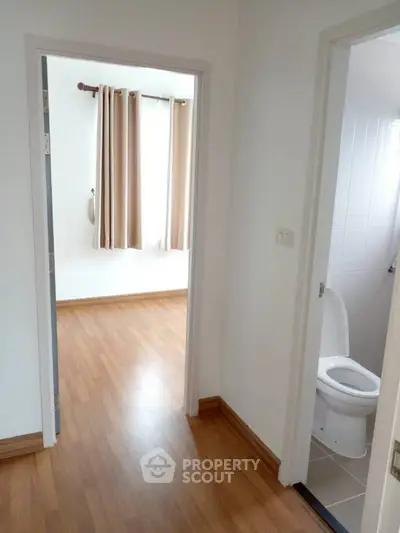 Bright hallway leading to a cozy bedroom and modern bathroom with wooden flooring.