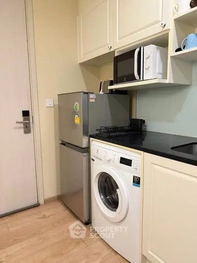 Compact kitchen with modern appliances including fridge, microwave, and washing machine in cozy apartment.