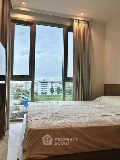 Cozy bedroom with large windows offering a stunning city view, perfect for relaxation and comfort.
