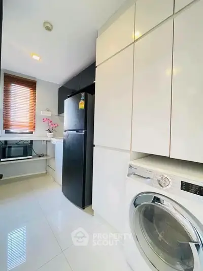 Modern kitchen with sleek appliances and ample storage space, featuring a washing machine and refrigerator.