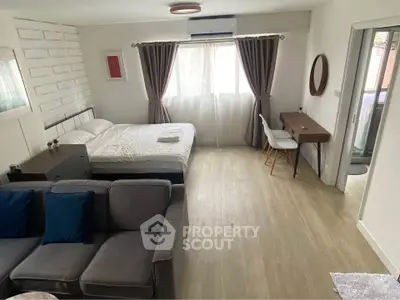 Modern studio apartment with cozy bed, stylish sofa, and elegant desk near balcony.
