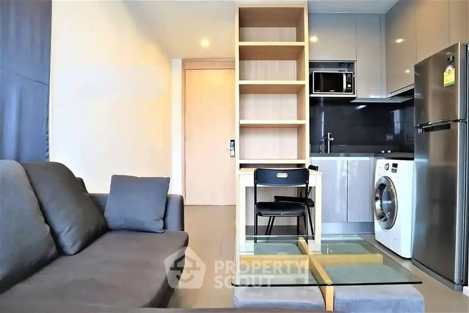Modern living room with integrated kitchen, featuring sleek appliances and stylish furniture.