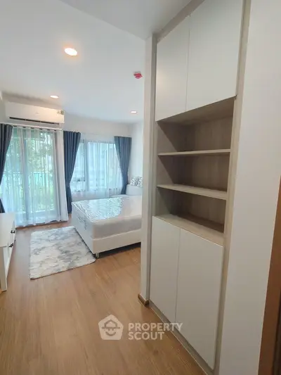Modern bedroom with large windows, wooden flooring, and built-in storage, offering a bright and cozy living space.