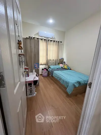 Cozy bedroom with wooden flooring and natural light, perfect for relaxation.