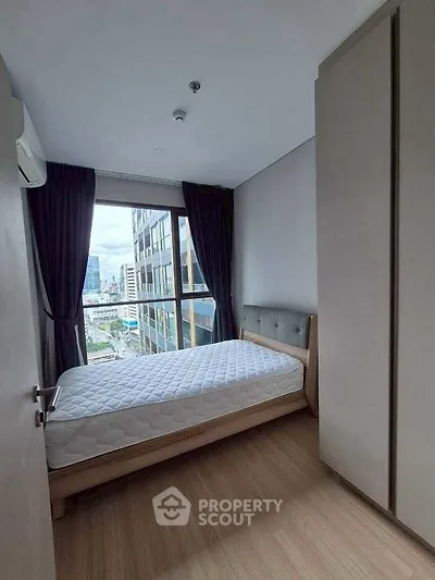 Modern bedroom with city view, featuring a comfortable bed and large window.